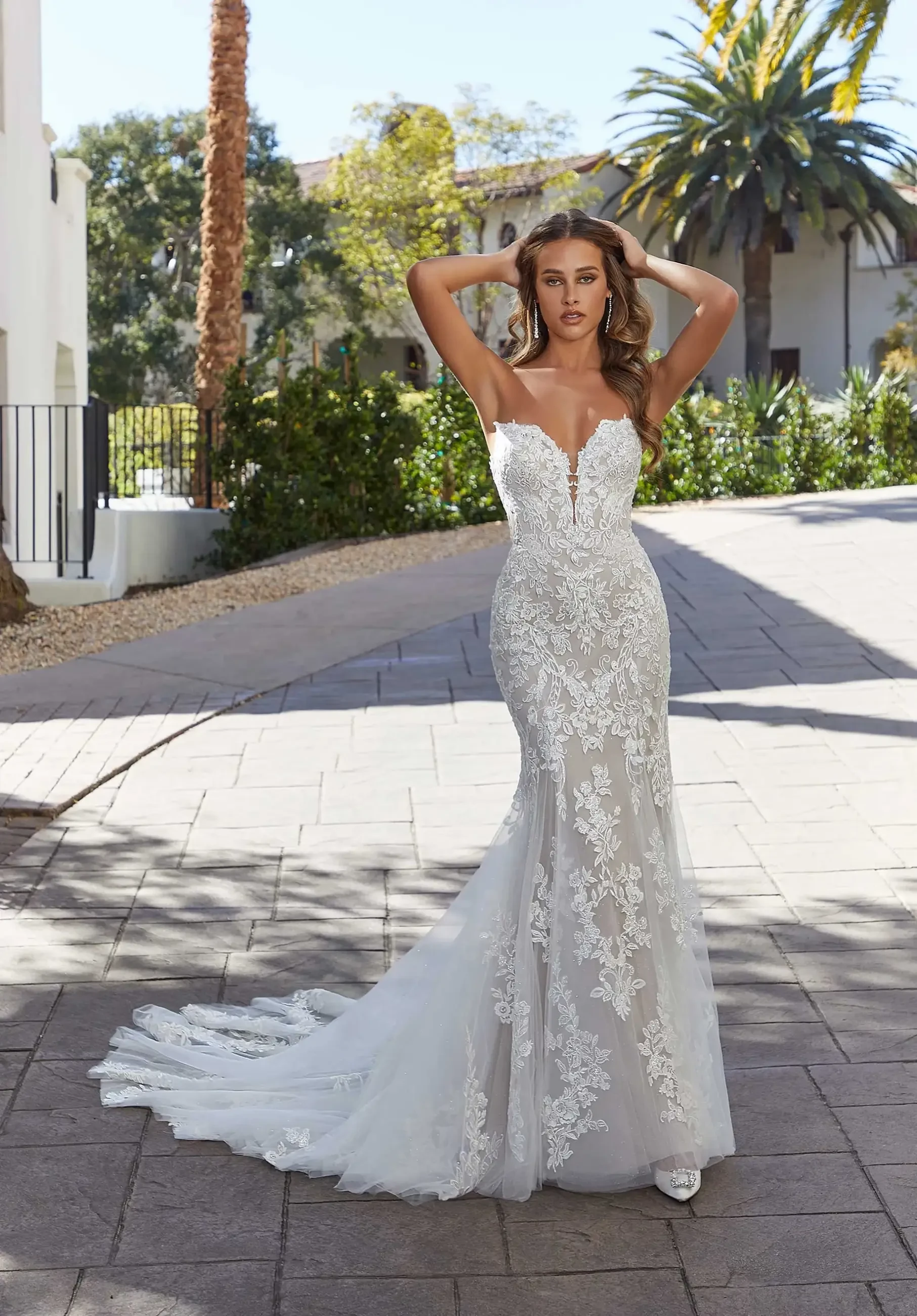 Model is wearing a sexy fit and flare gown with a plunging sweetheart bodice, intricate frosted, embroidered lace, an illusion back, and detachable whimsical bishop sleeves.
