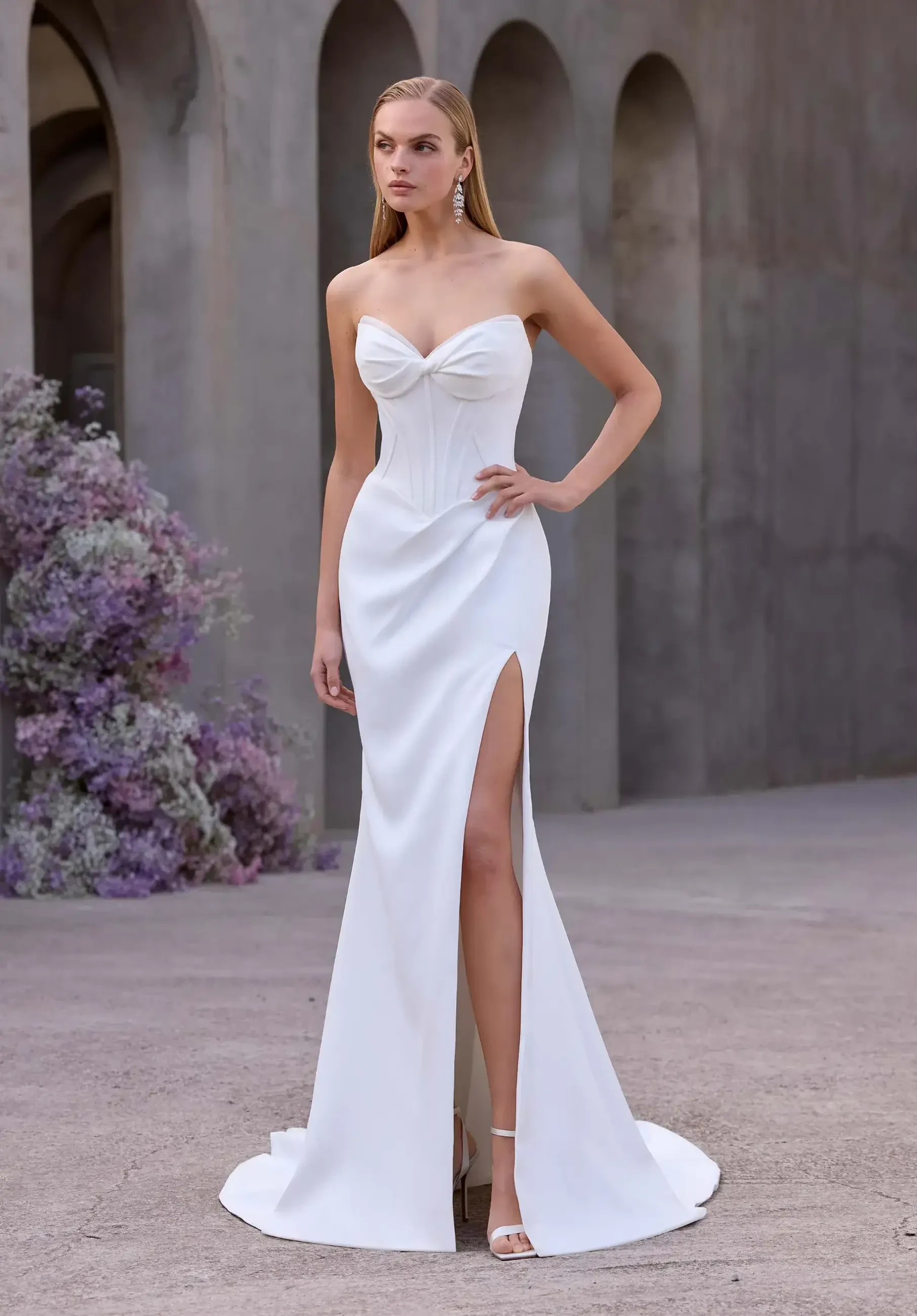 model is wearing a strapless sheath wedding dress with a slit