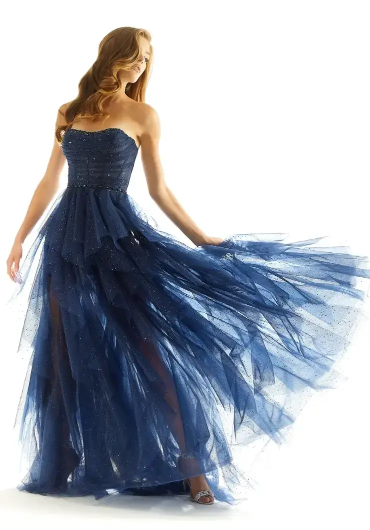 A model wearing a strapless, flowing navy blue gown made of layers of tulle fabric, captured in a graceful pose.