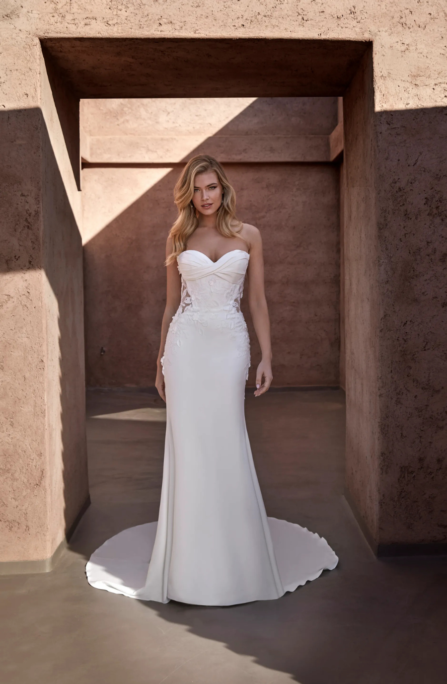 Model is wearing a strapless sweetheart fitted wedding gown with a gathered twist at the bodice 