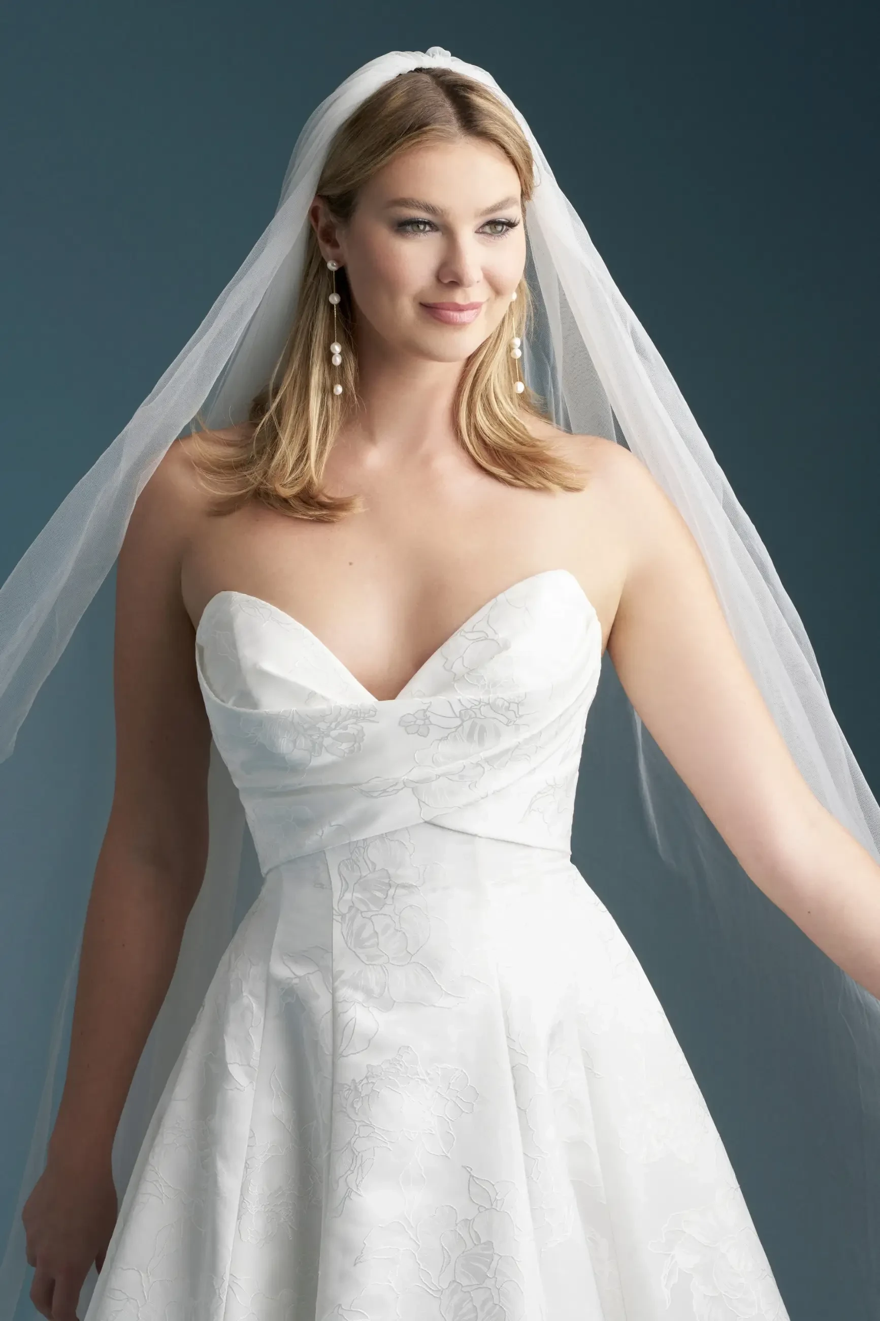 A woman wearing a white wedding dress and veil, smiling and looking to the side.