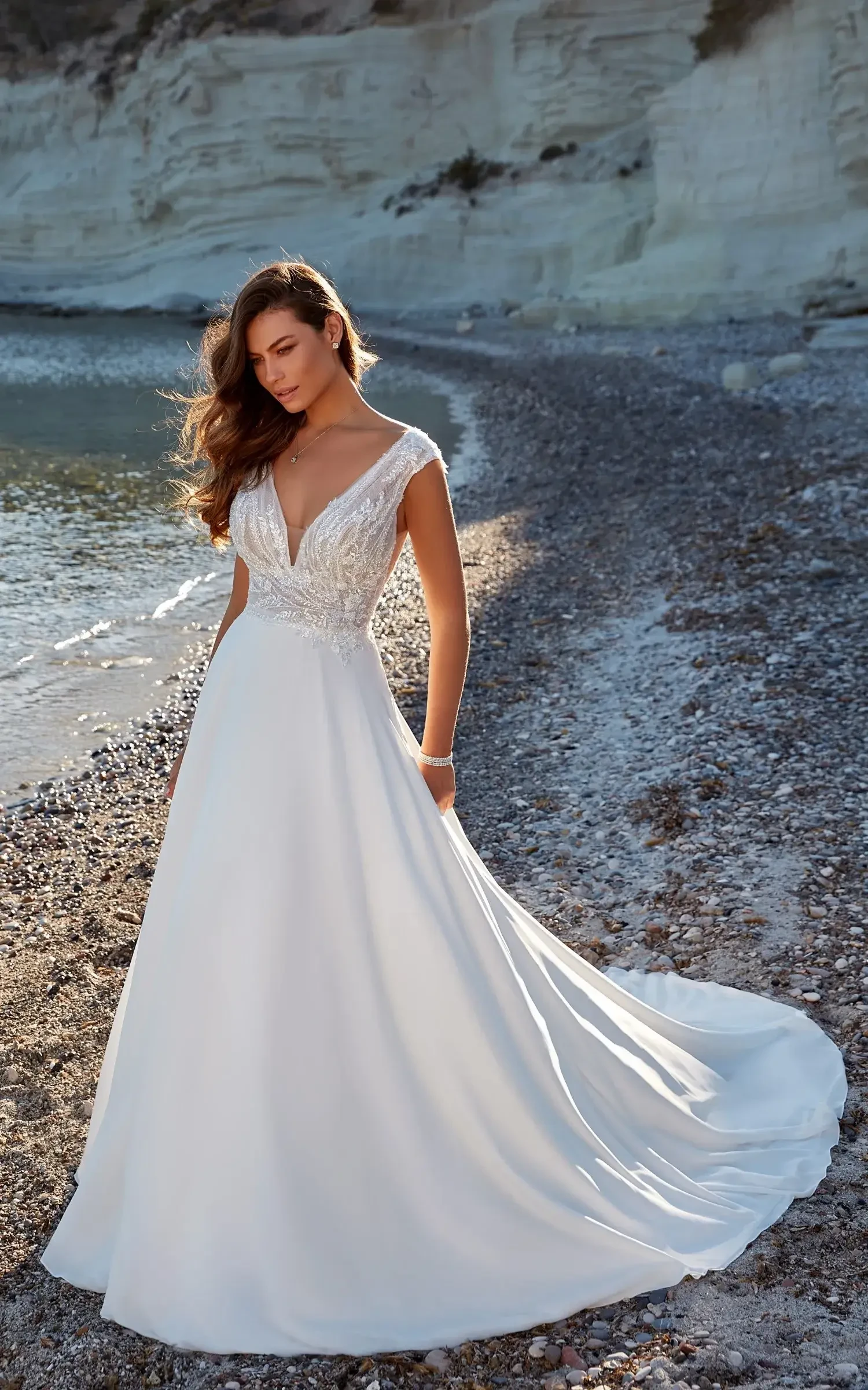 Model is wearing an a-line wedding dress with cap sleeves and a train