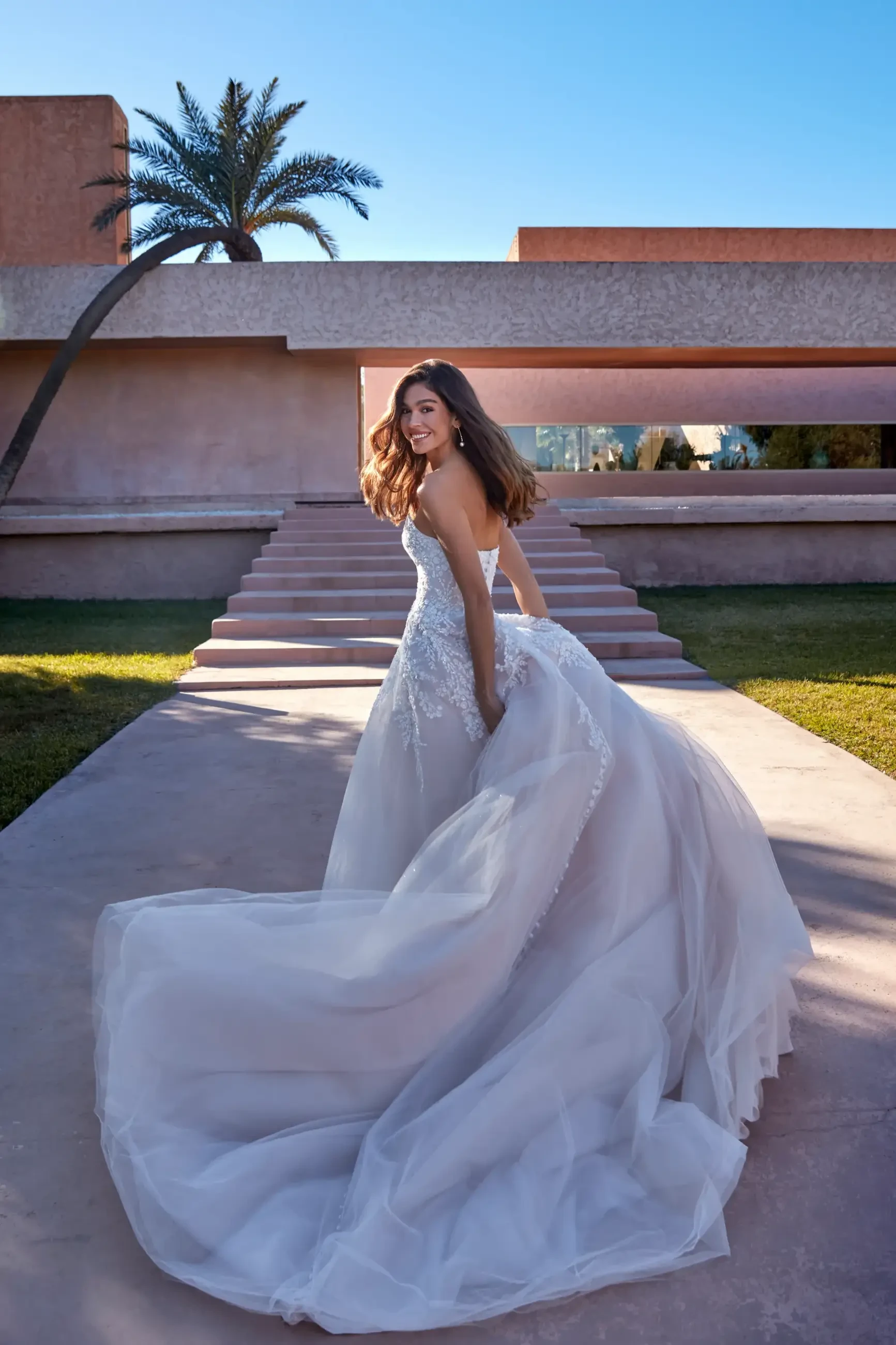 Model is wearing a dazzling A-line wedding dress with a pointed scoop neckline, delicately beaded lace appliques, layers of sparkle tulle, and covered buttons down the train.