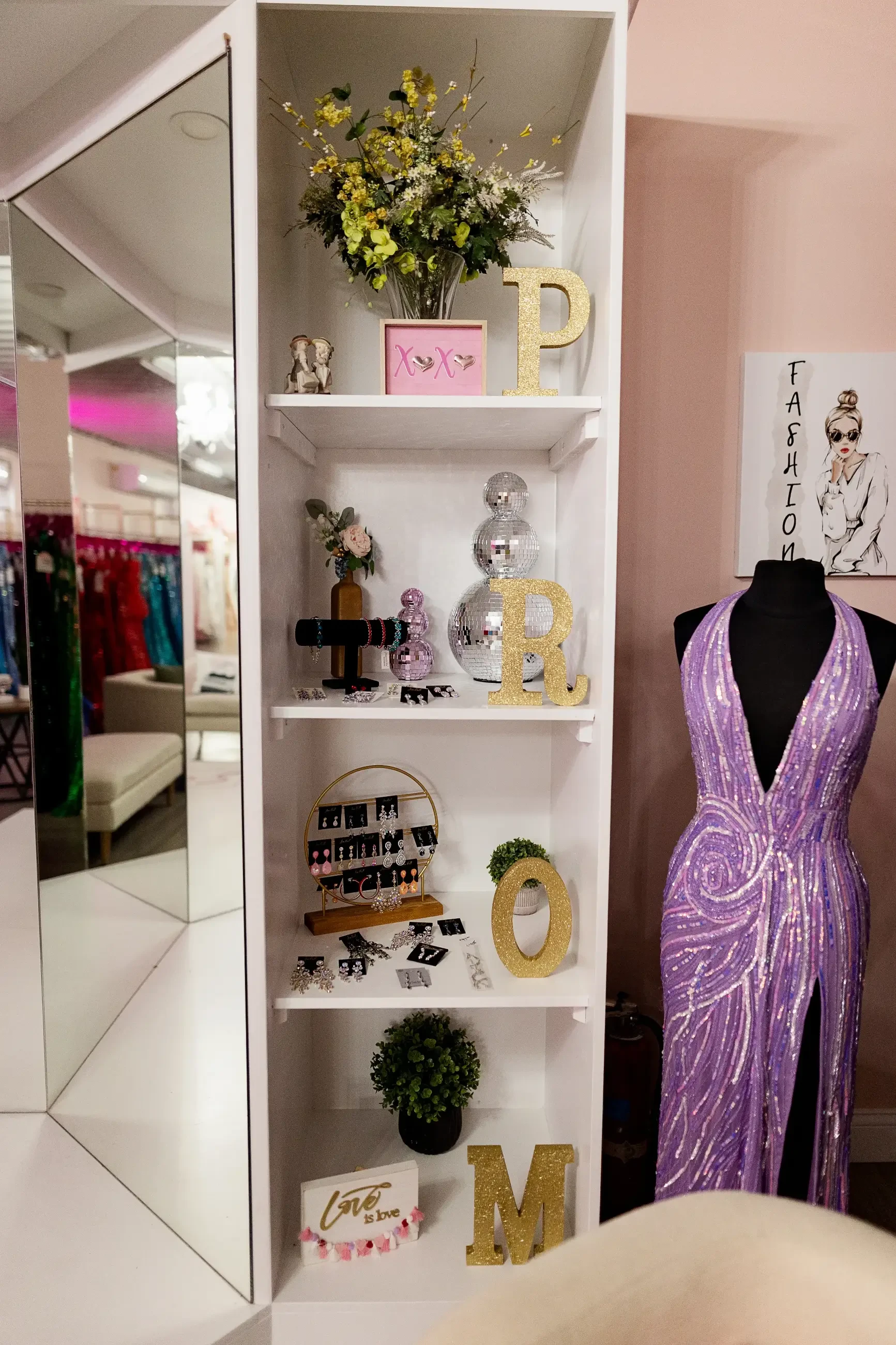 Boutique display with mirrored walls, decorative shelving, accessories, floral accents, and a