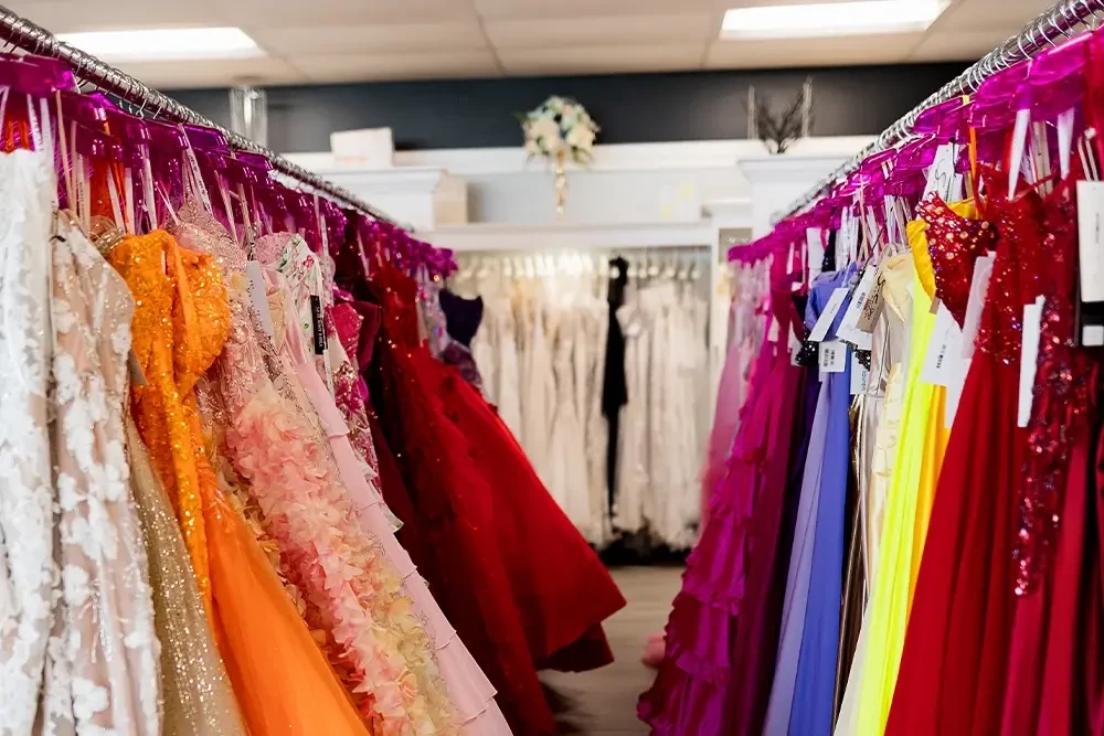 Rows of vibrant formal gowns in orange, red, pink, blue, and neutral tones displayed inside a dress